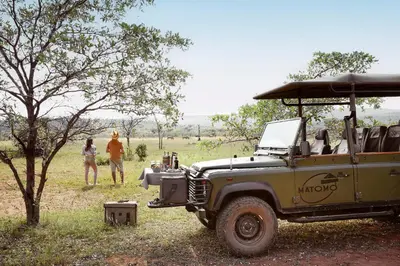 a military vehicle parked in a field with two people at Matomo Safari Lodge in Welgevonden Game Reserve