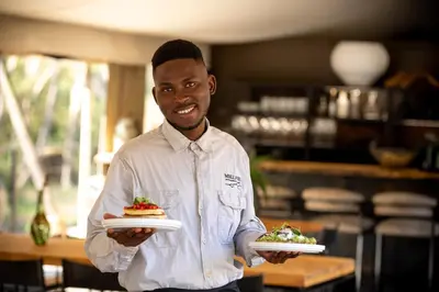 a man holding two plates with food on them at Mbizane Escarpment Retreat in Schoemanskloof