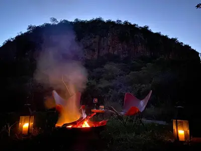 a fire in a field with two chairs and a table at Mbizane Escarpment Retreat in Schoemanskloof