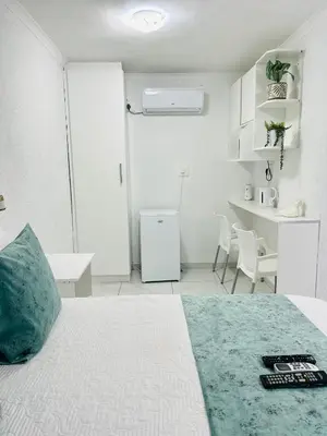 a white room with a bed and a kitchen at Duvha Guesthouse in Graskop