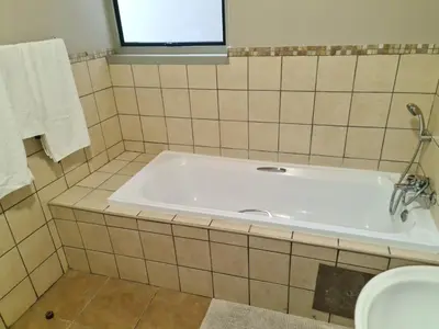 a bath tub in a tiled bathroom with a window at The Retreat, Midrand - 2bed 2bath in Midrand