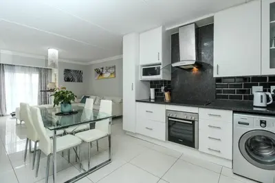 a kitchen with white cabinets and a table with white chairs at Gorgeous Diamond in Midrand