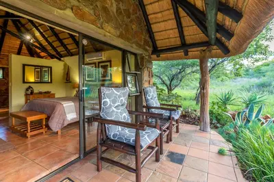 a room with a bed and chairs on a patio at Iketla Lodge in Ohrigstad