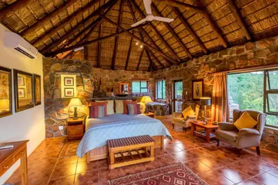 a bedroom with a bed and a stone wall at Iketla Lodge in Ohrigstad