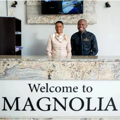 a man and woman standing behind a counter with the welcome to macarania sign at Magnolia Hotel in Middelburg