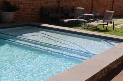 a swimming pool with blue water and chairs and a table at Magnolia Hotel in Middelburg