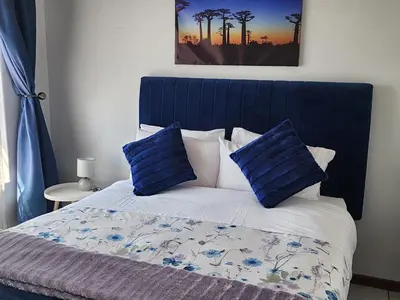 a bed with a blue headboard and two blue pillows at Faerie Glen Heights in Pretoria
