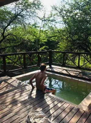 a man sitting on a wooden deck near a pool of water at Habibi Holiday Home in Marloth Park