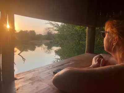 a woman sitting on a deck looking out at a lake at Panache Wildlife Cottage-Self Catering in Hoedspruit