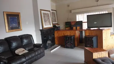a living room with a black leather couch and a television at Jay's Guest House in Witbank