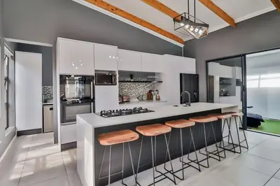 a kitchen with white cabinets and a counter with stools at House of Bongekile 4 Bed Luxury Home in Malelane in Malelane