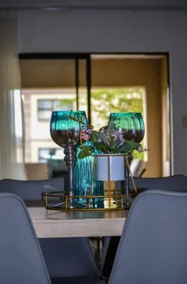 a table with two glasses and a vase with flowers at Peaceful gateaway - 2 bed apartment in Sunninghill with back-up power in Sandton