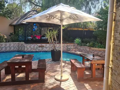 an umbrella and benches next to a swimming pool at Country Cabin in Midrand