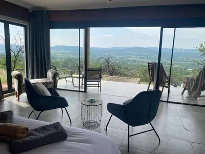 a bedroom with a bed and chairs and a large window at Rocky Road Mountain Lodge in Pretoria