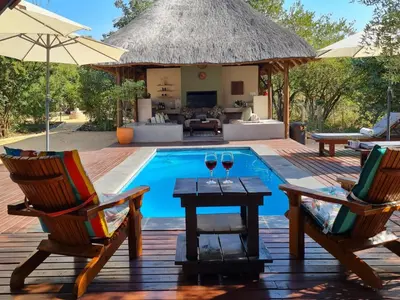 a pool with two chairs and a table with two glasses of wine at The Dreamcatcher Lodge in Hoedspruit