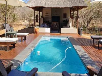 a swimming pool with chairs and a house at The Dreamcatcher Lodge in Hoedspruit