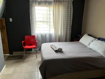 a bedroom with a bed with a red chair and a window at Mlakalaka Guesthouse in KuMcogwaba