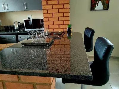 a dining table with black chairs and a brick wall at Modern 2 bedroom at Waterfall Ridge-Midrand in Midrand