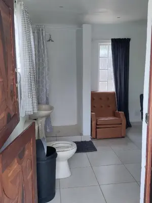 a bathroom with a toilet and a chair and a window at Outside room in Pretoria