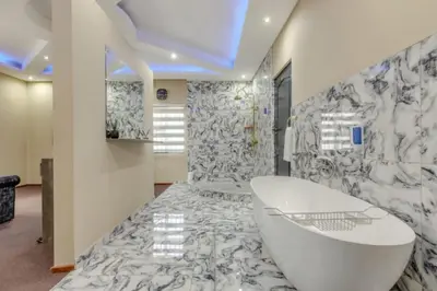 a bathroom with a white tub and a marble wall at Summit Della Suite in Centurion