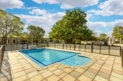 a swimming pool in a yard with a fence and trees at Summit Della Suite in Centurion