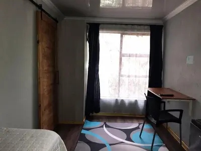 a bedroom with a bed and a desk and a window at Black Owl Lodge in Kempton Park
