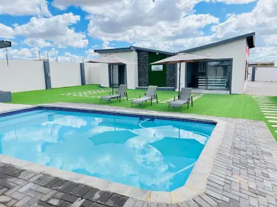 a swimming pool with chairs and a house at Reros Apartments in Mankweng in Mankweng
