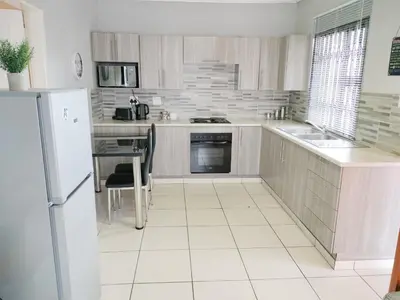 a white kitchen with a refrigerator and a table at Sunrise Guesthouse in Pretoria