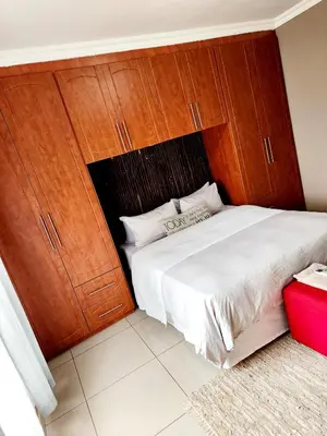 a bedroom with a large white bed with wooden cabinets at MAKWATAMBANI GUEST MANOR in Thohoyandou