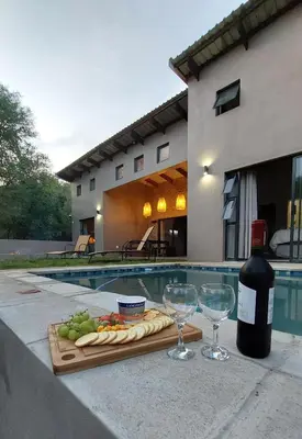 a bottle of wine and glasses on a table near a pool at Afri Villa Stays - Luxury Bush Villa Hyena in Marloth Park