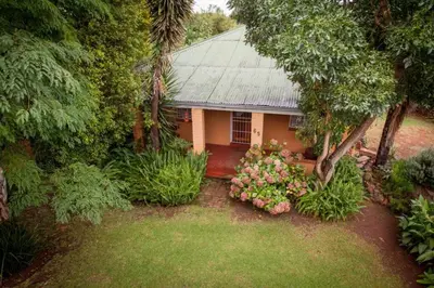 a small house with a tree and flowers in front of it at Climber's house in Waterval Boven