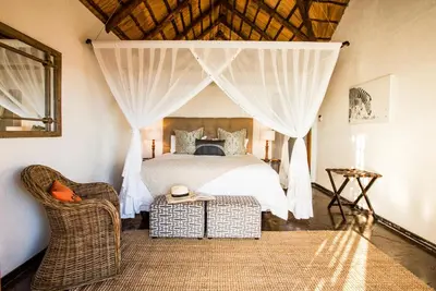 a bedroom with a bed with curtains and a chair at Magari Safari Villa in Vaalwater