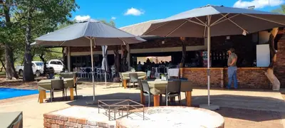 a man standing in front of a restaurant with tables and umbrellas at Mukumbura Swartwater in Swartwater