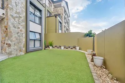 a backyard with a green lawn in front of a building at Modern 3-bed Garden Apartment in Waterfall in Midrand