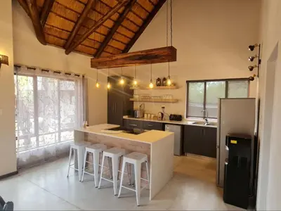 a kitchen with a counter with stools and a refrigerator at Hoedspruit Bush Stay in Hoedspruit