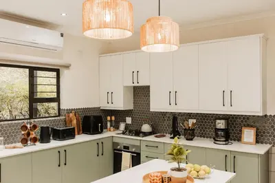 a kitchen with white cabinets and white counter tops at Chawal Stays Swartwitpens in Marloth Park