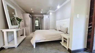 a white bedroom with a bed and a mirror at Montrose River Lodge in Schoemanskloof