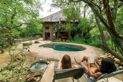 two women sitting in chairs by a swimming pool at Kruger Park Hostel in Marloth Park