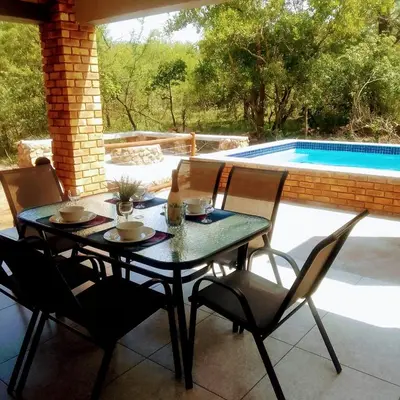 a table and chairs on a patio with a swimming pool at Sonador Bush House in Marloth Park
