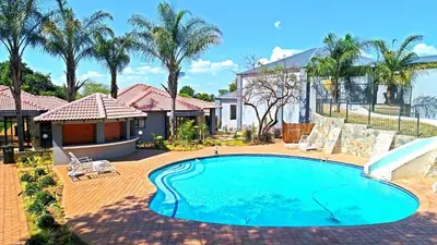 a swimming pool in front of a house with palm trees at Ultimate Sky _ 2 bedroom villa in Pretoria