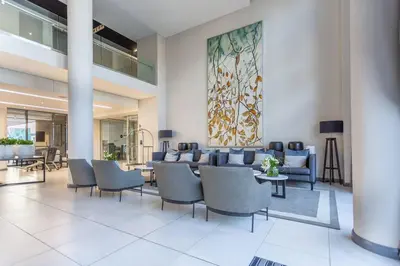 a lobby with chairs and tables and a painting on the wall at Menlyn Maine - The Trilogy Apartment 1111 in Pretoria
