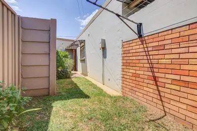 a brick wall next to a house with a yard at Ovendales Self Catering Cottage in Benoni
