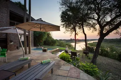 a patio with a wooden bench and an umbrella at Hippo Hills Lodge Ngwenya in Marloth Park