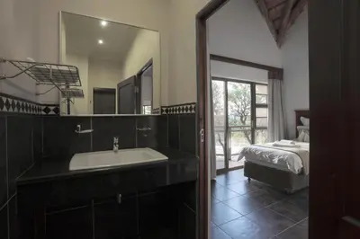 a bathroom with a sink and a mirror and a bed at Hippo Hills Lodge Ngwenya in Marloth Park