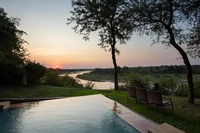 a swimming pool with two chairs next to a river at Hippo Hills Lodge Ngwenya in Marloth Park