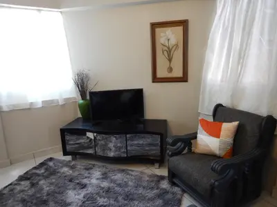 a living room with a tv and a chair and a table at Solitaire Guest Apartments in Pretoria
