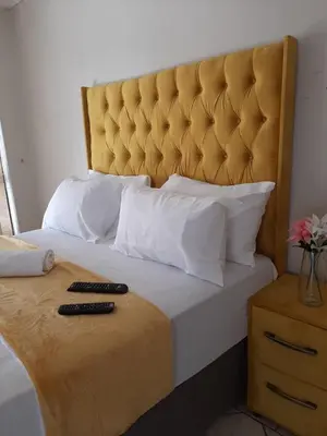 a bed with a yellow headboard and two remote controls on it at Brovad Guesthouse in Kempton Park