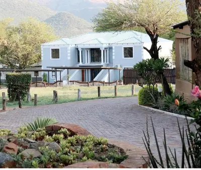 a white house with a tree and a brick driveway at Lesolo Lodge in Burgersfort