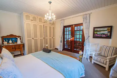 a bedroom with a bed and a chair and a chandelier at Crossroads Cottage in Dullstroom