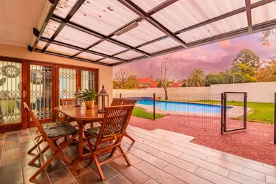 a patio with a table and chairs and a swimming pool at Greencroft Villa in Kempton Park